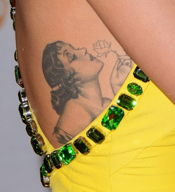 Rita Ora flaunts her intricate pinup girl tattoo on her ribcage, accentuated by a dazzling yellow gown