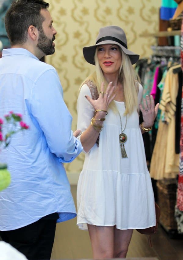 Tori Spelling enjoys a conversation while flaunting her boho-chic outfit with a white babydoll dress and stylish accessories