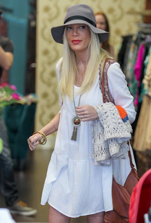 Tori Spelling showcases her boho-chic style in a white babydoll dress, accessorized with a gray hat and layered jewelry