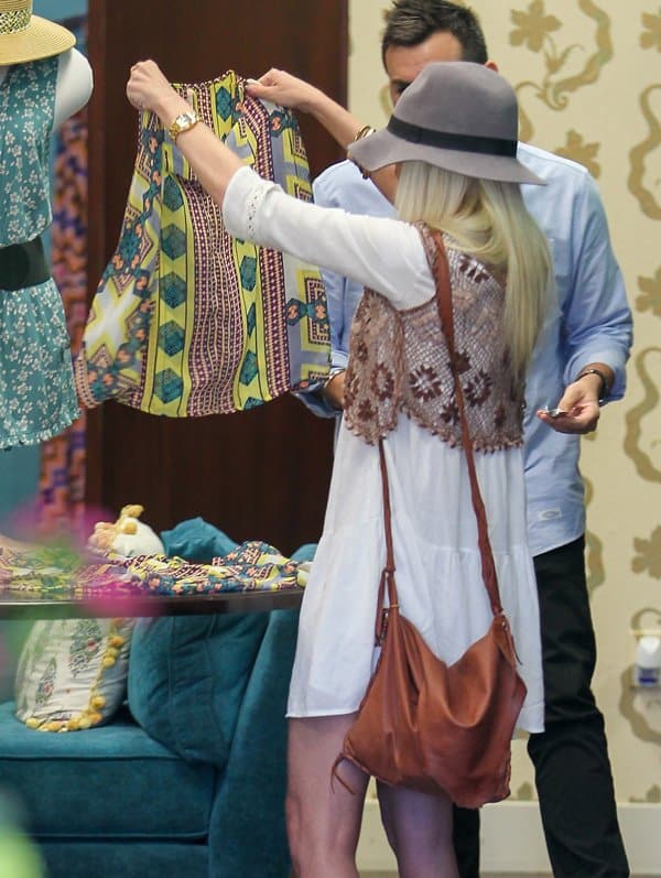 Tori Spelling examines a colorful top, enhancing her bohemian look with a crocheted vest and stylish accessories