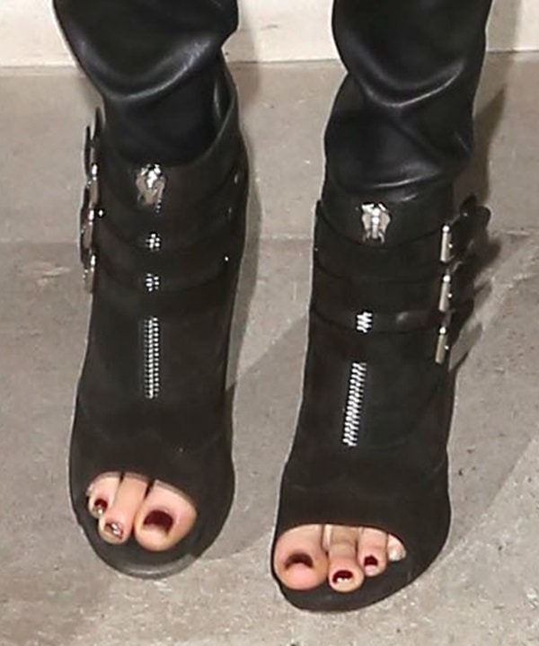 Cara Delevingne showcased a stylish burgundy pedicure in black suede Tabitha Simmons "Eva" booties featuring edgy zipper detailing, multiple buckled straps, and chic open-toes
