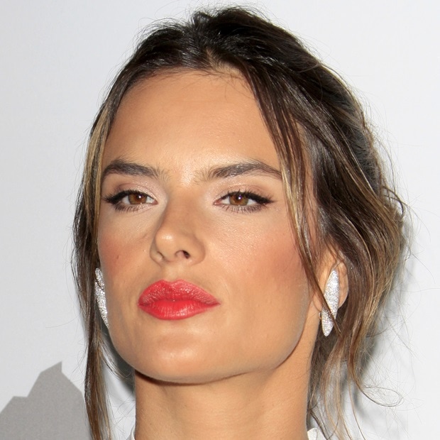 Alessandra Ambrosio showcases a sleek, textured updo with soft strands framing her face, paired with bold red lips for a glamorous finish