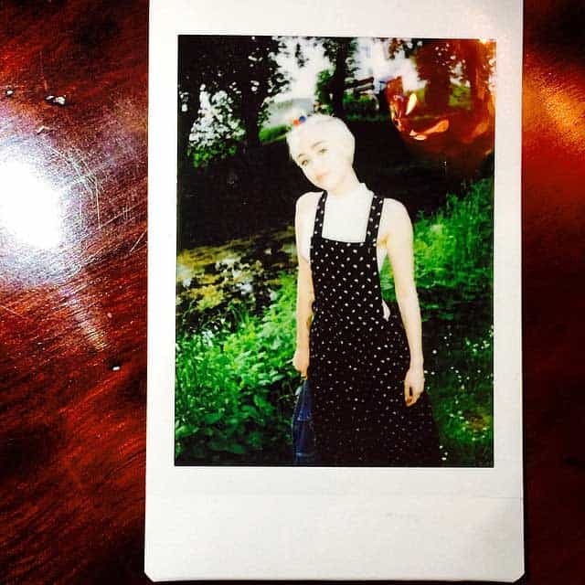 Miley Cyrus showcases her eccentric style in a black printed overall dress paired with a white crop top and a colorful pompom hairband