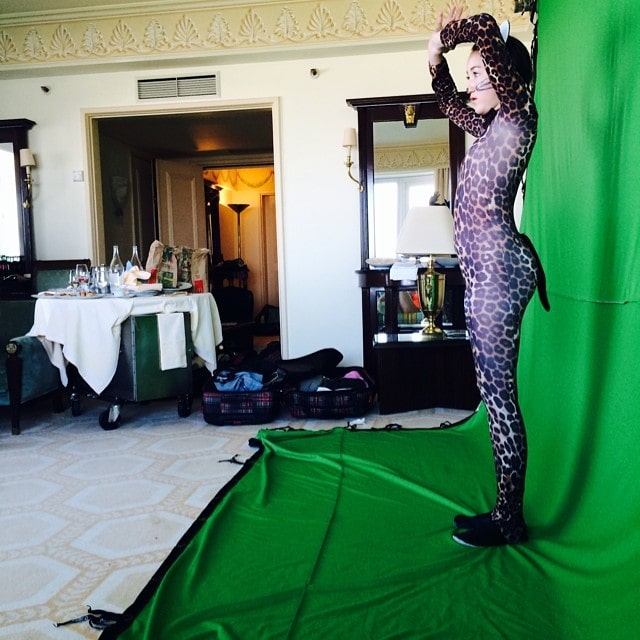 Noah Cyrus poses confidently in a leopard-print catsuit against a green screen, showcasing her playful side during a behind-the-scenes moment