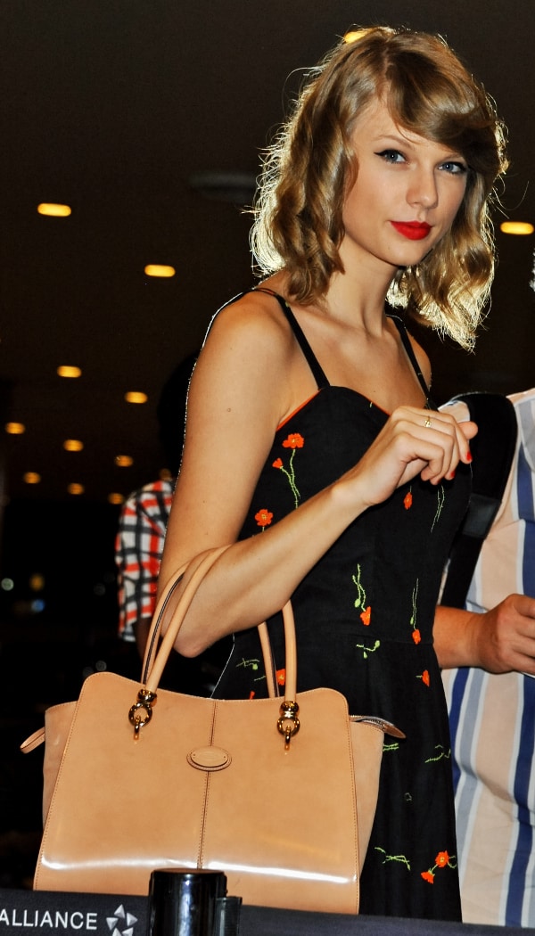 Taylor Swift exudes retro glamour with her large curls, bright red lips, and a black dress adorned with orange pansies, paired perfectly with a cream Tod's 'Sella' tote