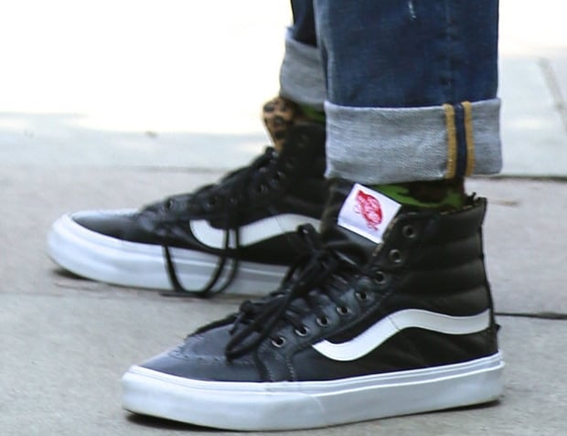 Gwen Stefani adds a cool, casual edge to her look with black leather Vans Sk8-Hi sneakers featuring the brand’s signature white side stripe, a high-top silhouette, and leopard-print sock detail peeking through