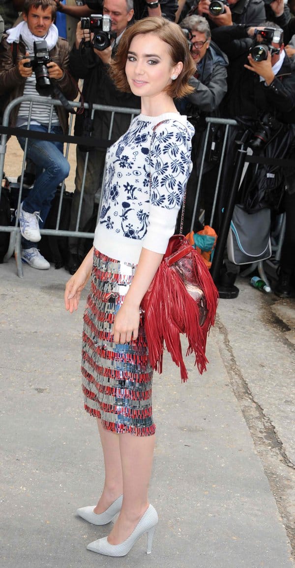 Lily Collins wore a monochrome crew-neck jumper paired with an elegant tiered pencil skirt featuring ruby red fringing