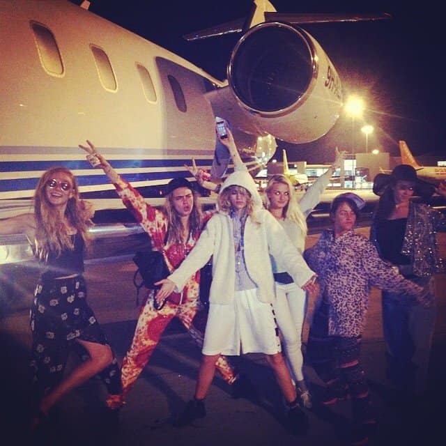 Cara Delevingne and friends strike a pose in playful outfits, including her pepperoni pizza-print jumpsuit, in front of a private jet