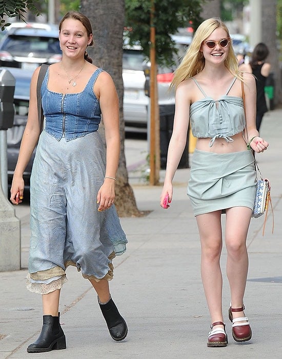 Elle Fanning having laughs with a friend in matching denim outfits while showing off her playful style with a midriff-baring top and a colorful Rebecca Minkoff bag