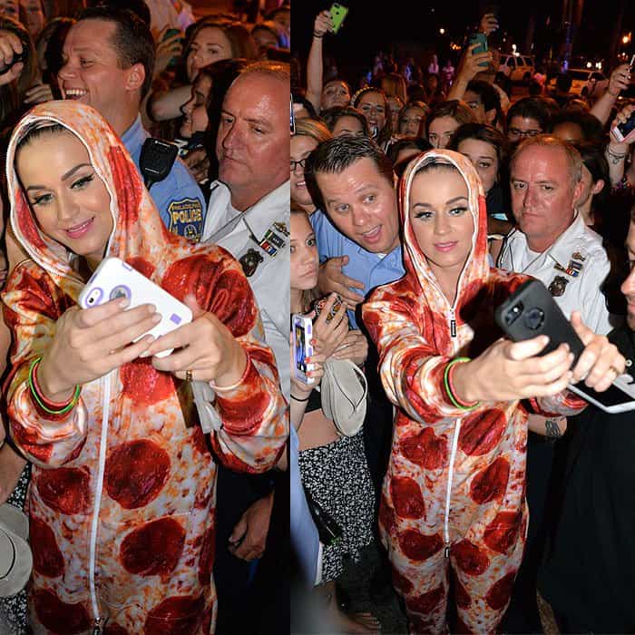 Katy Perry poses for selfies with fans while rocking a pepperoni pizza-print jumpsuit, surrounded by a crowd
