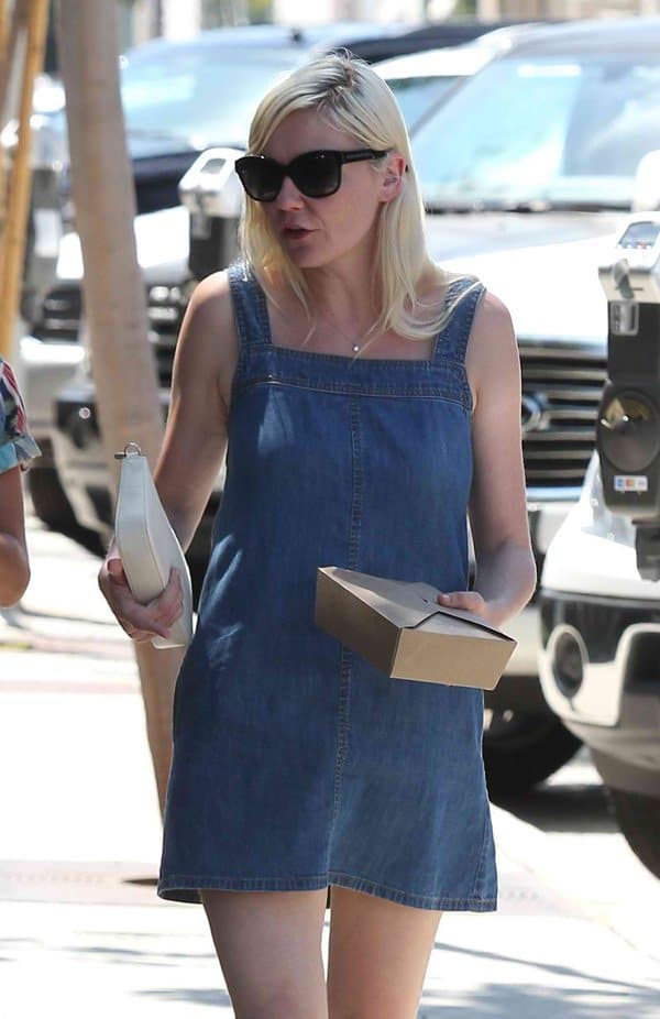 Kirsten Dunst wearing a denim summer dress and holding a white clutch while running errands in Los Angeles