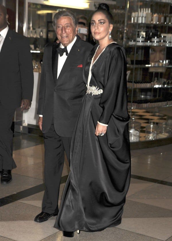 Lady Gaga exudes elegance in a black rhinestone-detailed caftan with an intricate waist accent, pairing the flowing gown with towering black platform heels for a dramatic red carpet statement