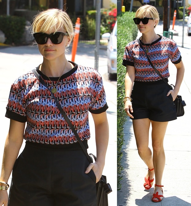 Reese Witherspoon pairs a vibrant textured top with chic black shorts, finishing the look with bold red strappy heels for a playful yet polished summer vibe