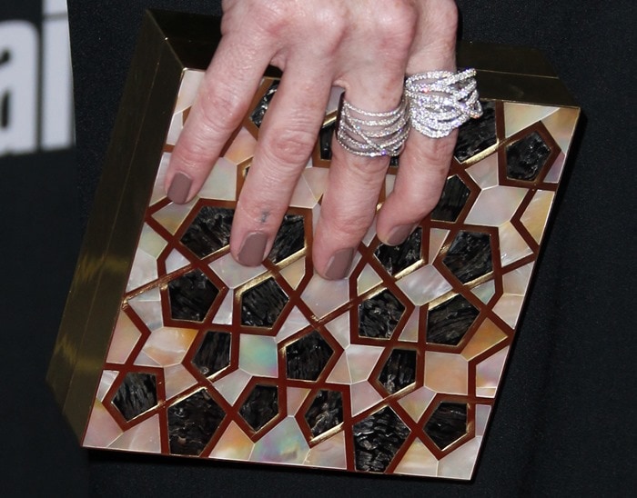 Taryn Manning toting a geometric Atelier Strut clutch with a mosaic-like inlay of iridescent shell, black stone, and metallic accents, paired with stacked diamond rings and taupe matte nail polish