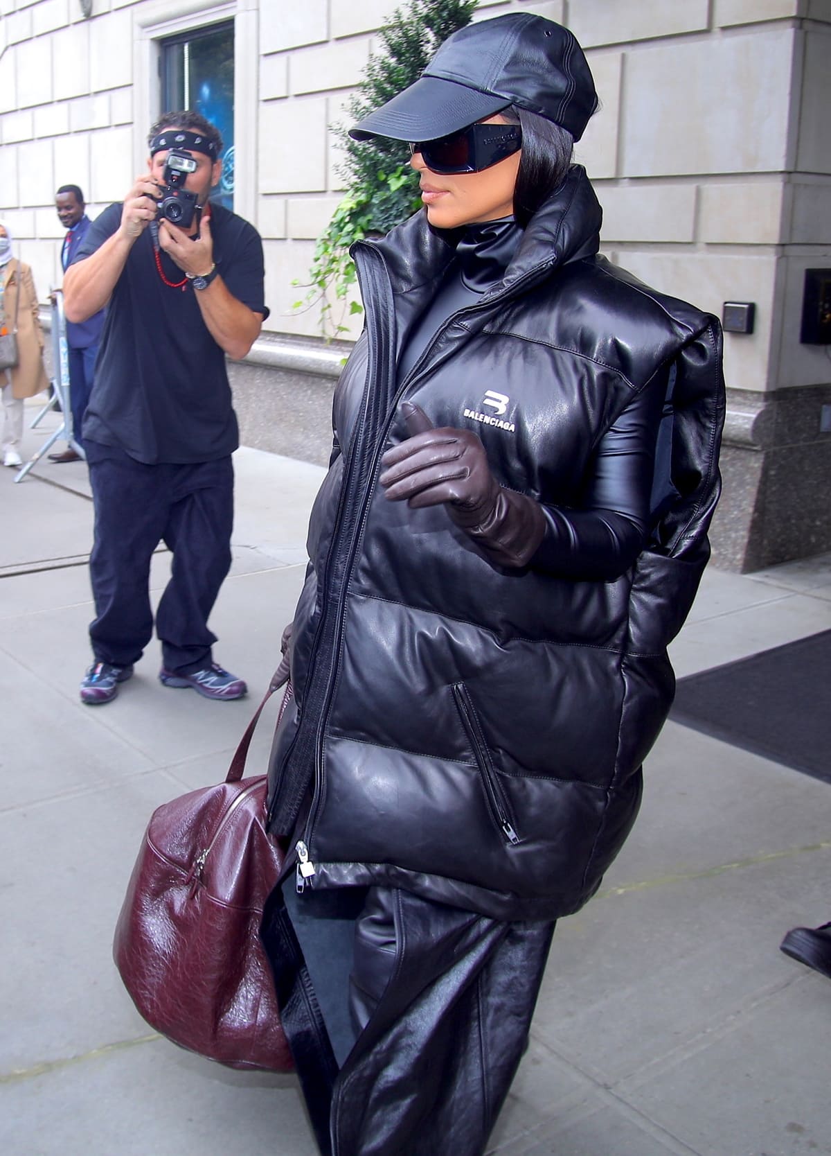 Kim Kardashian wears a puffy black Balenciaga vest with burgundy gloves and a leather baseball cap