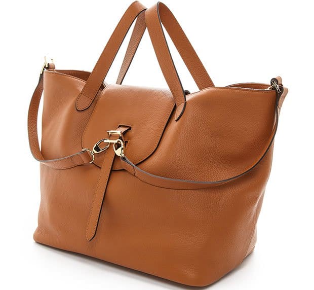 This large caramel brown leather tote bag features a spacious main compartment, a decorative gold-tone clasp with strap detail, sturdy top handles, and a detachable shoulder strap for versatility
