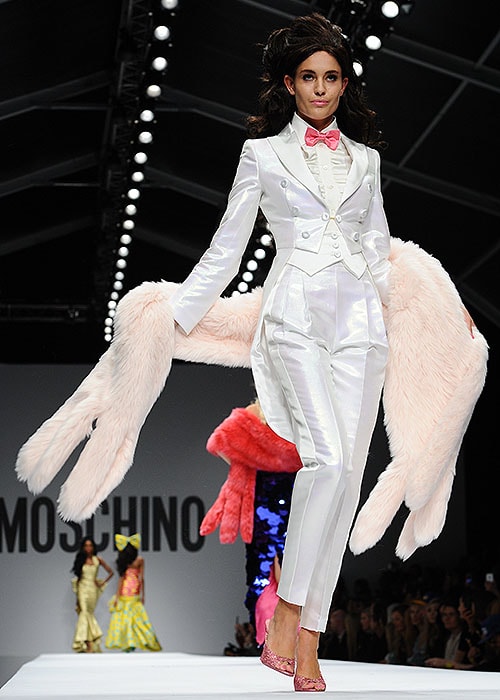 A model walks the runway in a sleek white satin tuxedo with a pink bow tie and oversized pink fur stole, part of Moschino's Spring 2015 Barbie-inspired collection
