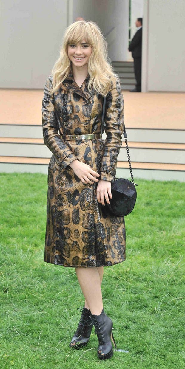 Suki Waterhouse looks chic in a gold and black python-skin trench coat dress, paired with lace-up black ankle boots and a stylish round handbag