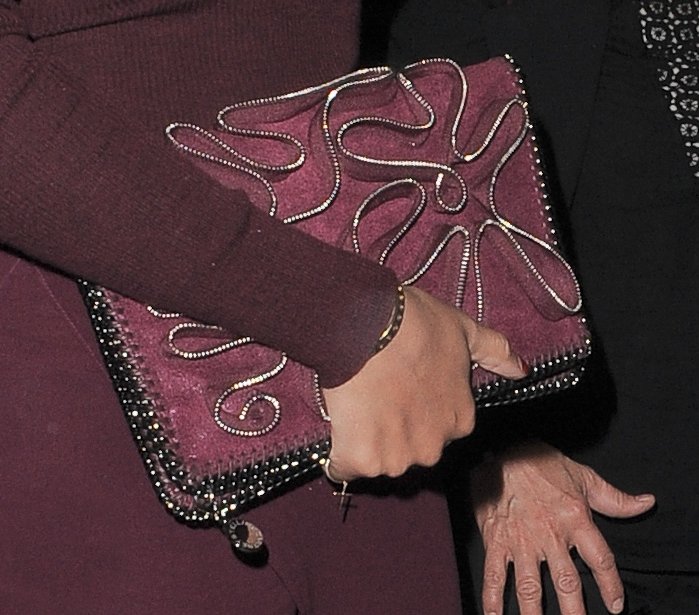 Beyoncé carries a textured burgundy Stella McCartney "Falabella" clutch adorned with swirling metallic piping and beaded trim, adding a bold, artistic flair to her monochrome look