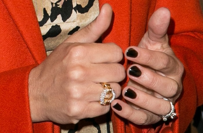 Julia Roberts showcases her chic style with glossy black nail polish, sparkling statement rings, and a bold orange coat