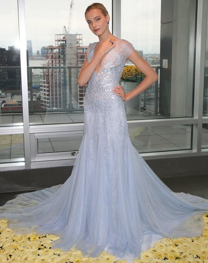 The light blue gown features intricate beading on a fitted bodice, cap sleeves, and a plunging neckline, flowing into a dramatic tulle skirt with a train