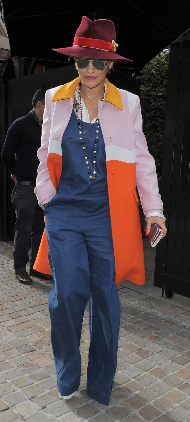 Rita Ora wears a colorful Prada Spring 2014 coat with denim overalls, Acne Studios sunglasses, a Chanel necklace, and a burgundy fedora