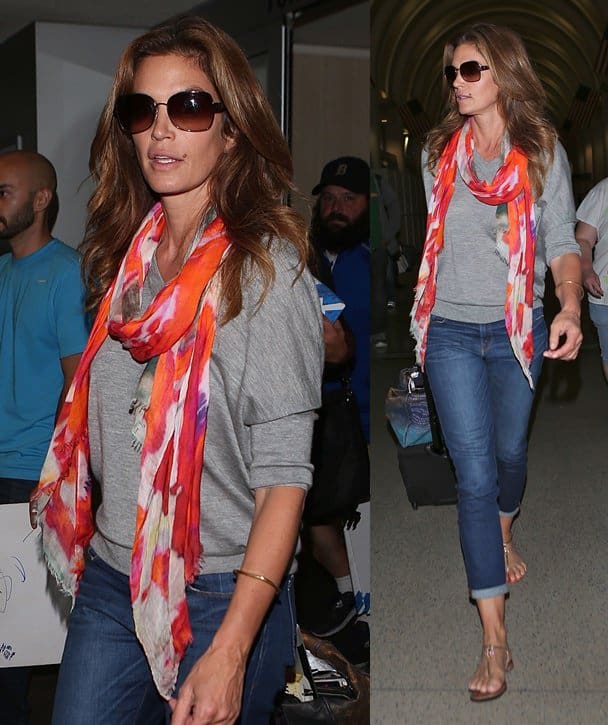 Cindy Crawford looked effortlessly chic in a simple sweater paired with jeans, accessorized with a printed scarf, sunglasses, and flat thong sandals