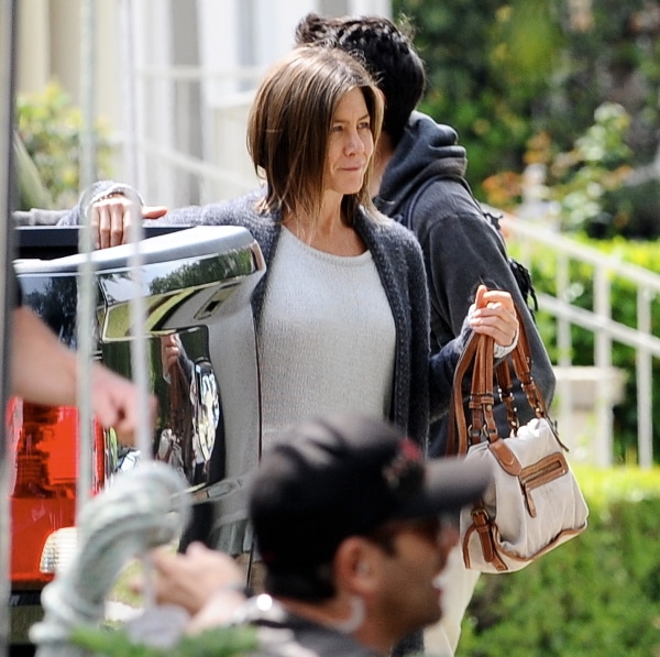 Jennifer Aniston wearing a flimsy knitted white top underneath a loose grey cardigan