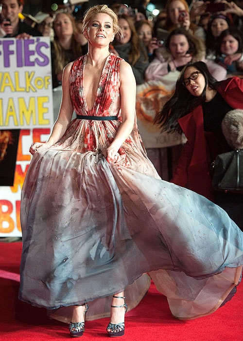 Elizabeth Banks adjusting the skirt of her gown and showing her shoes from underneath the hemline