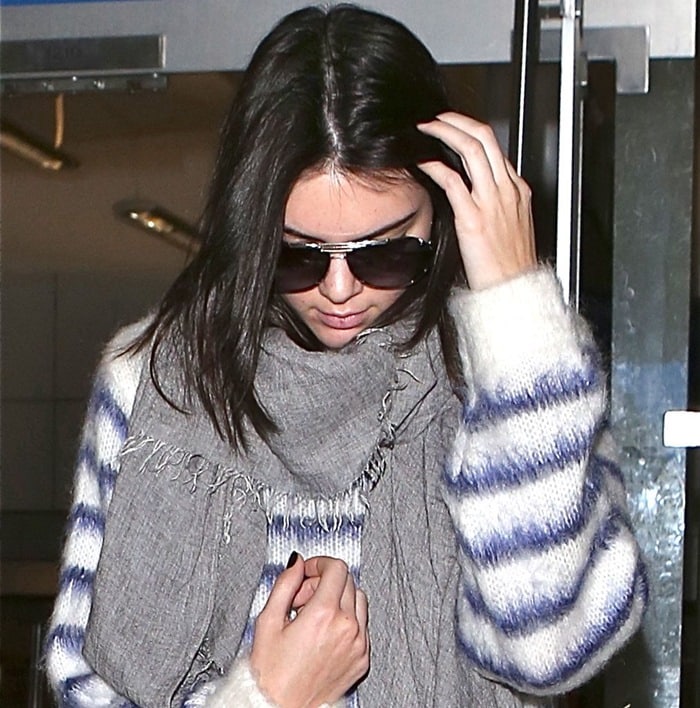 Kendall Jenner conceals her acne with sunglasses while wearing a cozy striped sweater and gray scarf at LAX