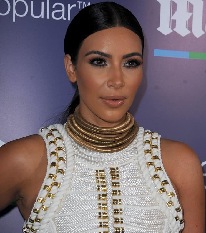 Kim Kardashian styled her custom Balmain dress with an eye-catching gold choker necklace, sleek pulled-back hair, and natural makeup, perfectly complementing the intricate details of her stunning outfit
