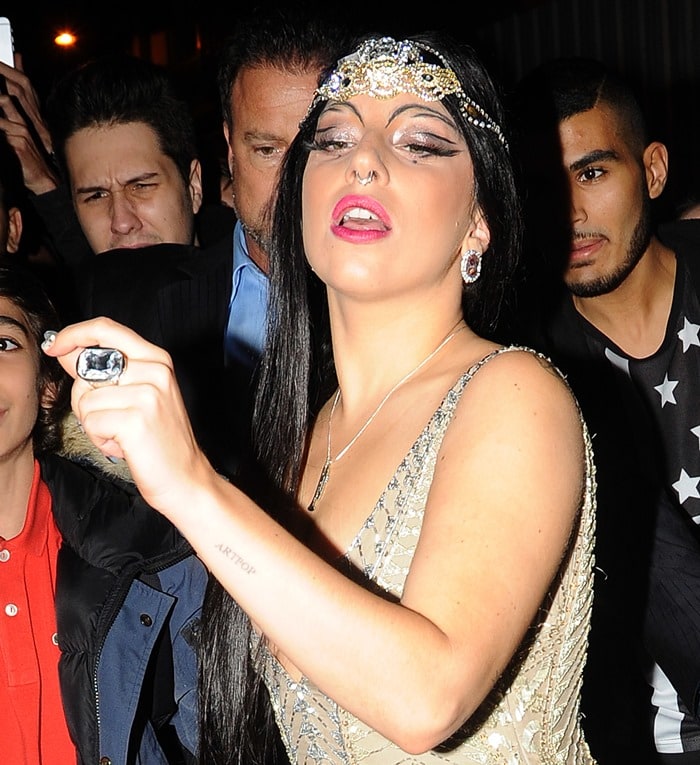 Lady Gaga channels vintage glamour with a jeweled headpiece, bold cat-eye makeup, shimmering earrings, and a statement cocktail ring that completes her opulent 1920s-inspired look