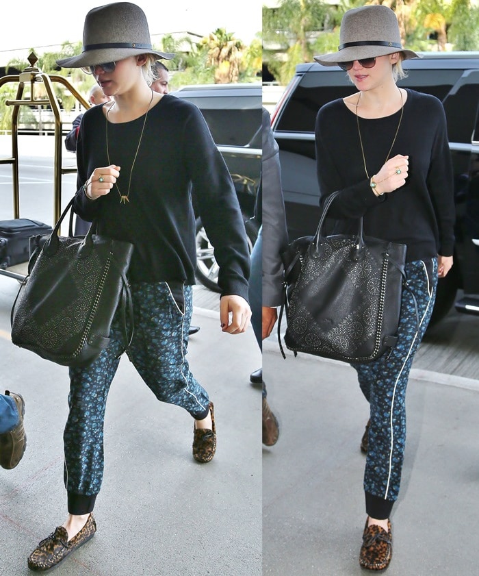 Hunger Games star Jennifer Lawrence wearing a mismatched outfit consisting of a wide-brimmed hat, oversized sunglasses, loose-fitting tapered black trousers with a blue floral design, and leopard-print moccasins