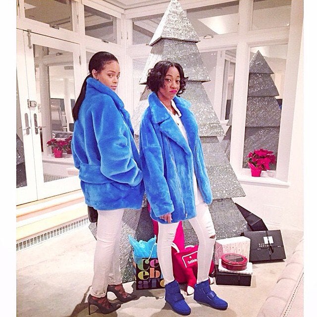 Rihanna and her BFF, Melissa Forde, show off their coordinated holiday looks in vibrant faux fur coats, white jeans, and contrasting footwear—lace-up heels for Rihanna and blue ankle boots for Melissa—standing stylishly in front of a shimmering crystal-encrusted tree