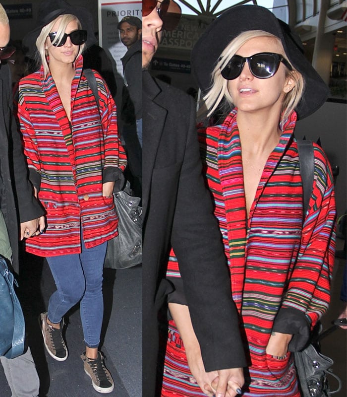 Ashlee Simpson at the airport, wearing a red striped coat, skinny jeans, leopard print sneakers, oversized sunglasses, and a fedora hat