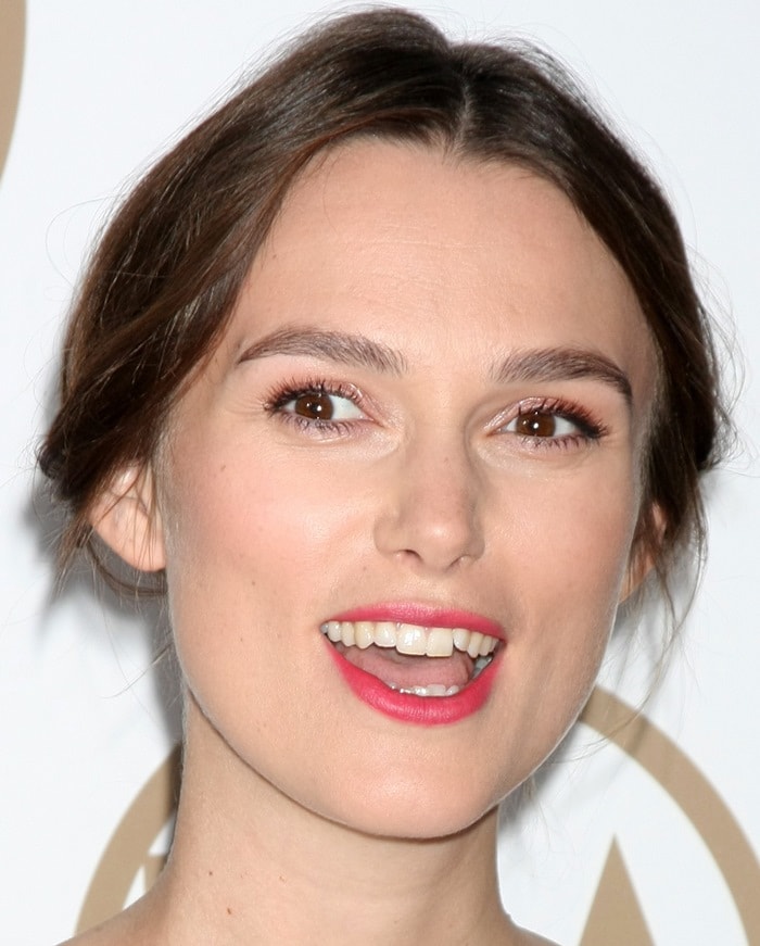 Keira Knightley wears a romantic center-parted updo paired with bright pink lipstick and softly defined eyes