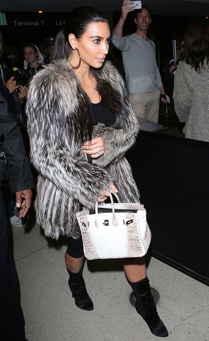 Kim Kardashian steps out in a luxurious fur coat paired with black leggings, heeled boots, and a striking white crocodile Hermès Birkin bag, exuding a chic, winter-ready look