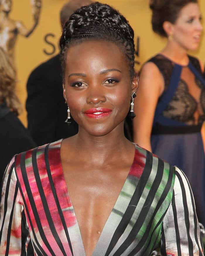 Lupita Nyong’o stuns in a multicolored Elie Saab gown with bold black stripes, paired with a braided updo and vibrant red lipstick, at the 2015 SAG Awards