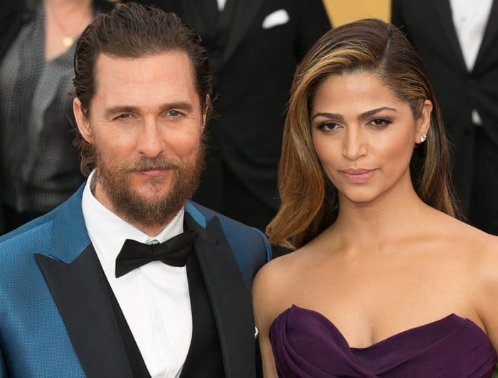 Camila Alves dazzles in a strapless aubergine gown with sleek, side-parted hair, standing next to Matthew McConaughey in a sharp blue tuxedo