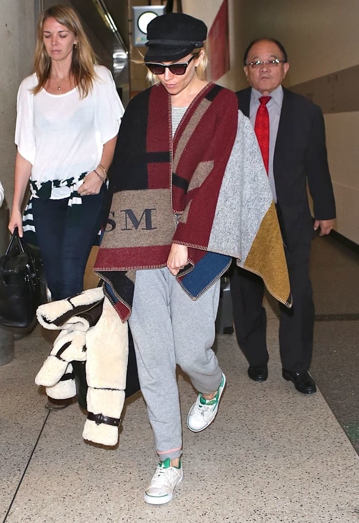 Sienna Miller sported a cozy yet fashionable outfit consisting of a gray sweater and sweatpants and accessorized with a hat, sneakers, and a personalized Burberry blanket wrap