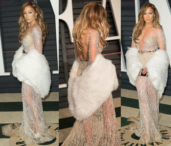 Jennifer Lopez dazzled in a sheer, embellished Zuhair Murad gown, styled with a luxurious white fur stole, elegant wavy hair, and sparkling drop earrings, creating a stunning and glamorous look at the 2015 Vanity Fair Oscar Party