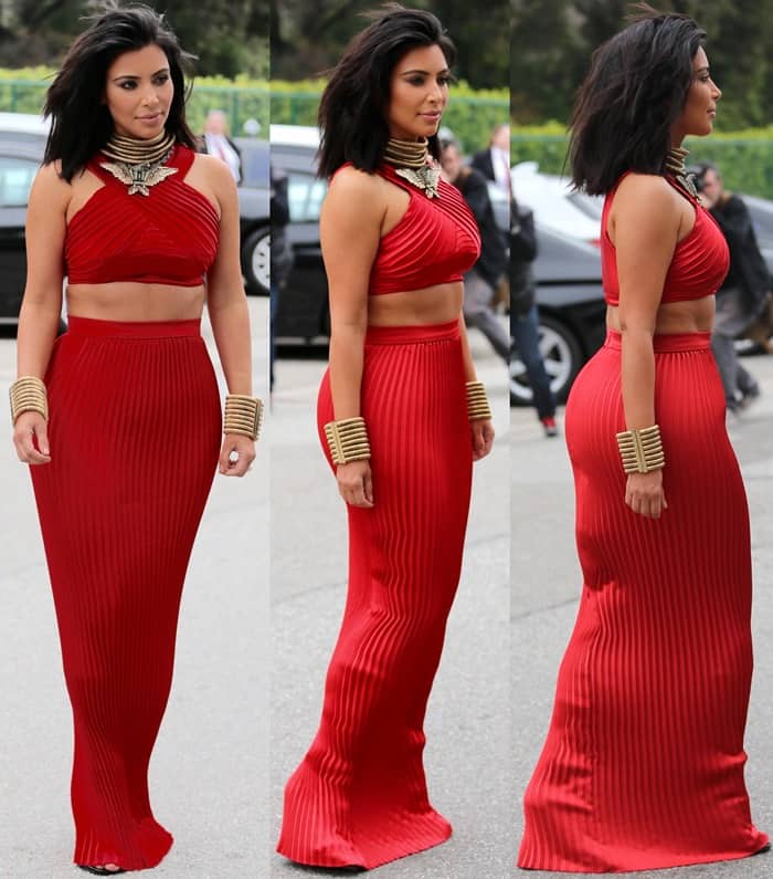 Kim Kardashian stuns in a vibrant red Balmain crop top and pleated maxi skirt, accessorized with gold bracelets and a statement necklace, showcasing her new short haircut at the Roc Nation Pre-Grammy Brunch