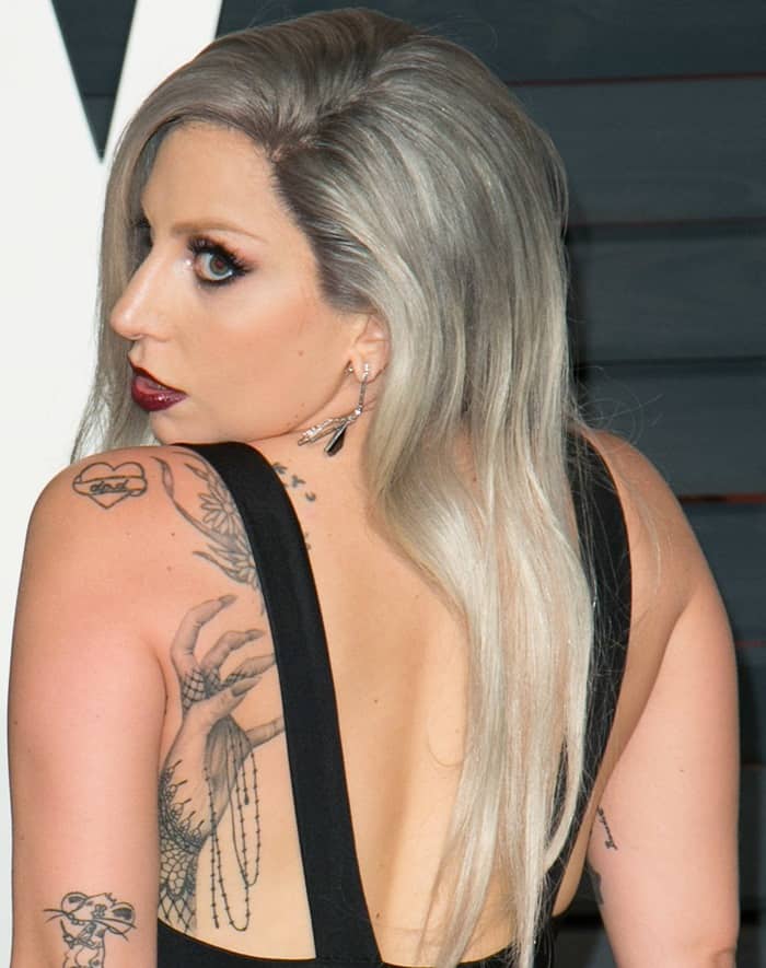 Lady Gaga showcased her back tattoos, including a detailed hand-turned-monster paw tattoo and intricate line art, adding an edgy touch to her look at the 2015 Vanity Fair Oscar Party