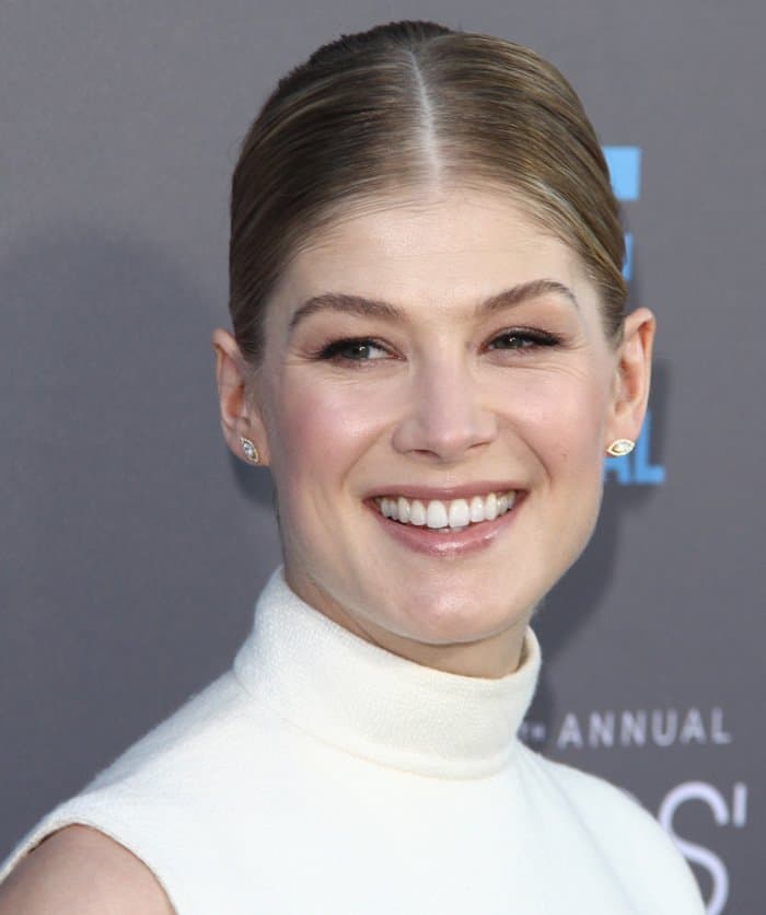 Rosamund Pike styled her look with a sleek, high-neck white dress, complemented by minimalist jewelry and a smooth, low bun