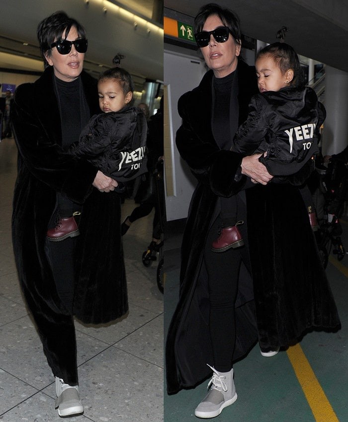 Kris Jenner, wearing a pair of Kanye West x Adidas Originals Yeezy 750 Boost, arrives at Heathrow Airport carrying baby North West, who was wearing a 'Yeezus Tour" bomber jacket in support her father Kanye on March 2, 2015