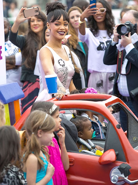 Rihanna grinning while posing with kids on the purple carpet