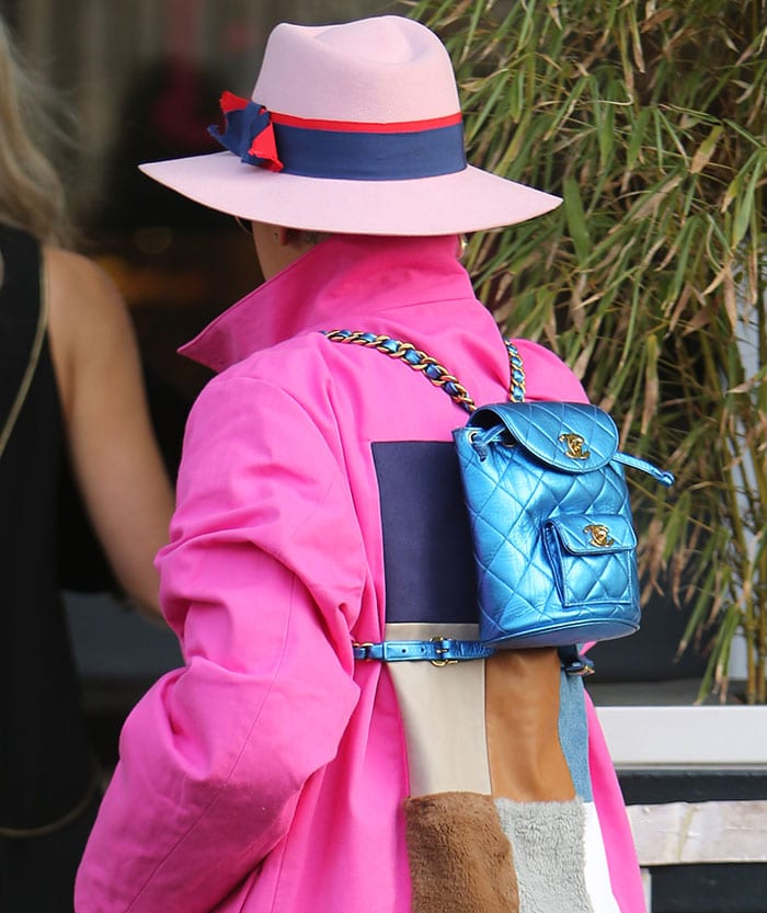 Rita Ora styled her look with a striking metallic blue Chanel mini backpack, featuring the brand’s signature quilted leather, gold-tone hardware, and a chain-accented strap that popped against her bold pink patchwork coat