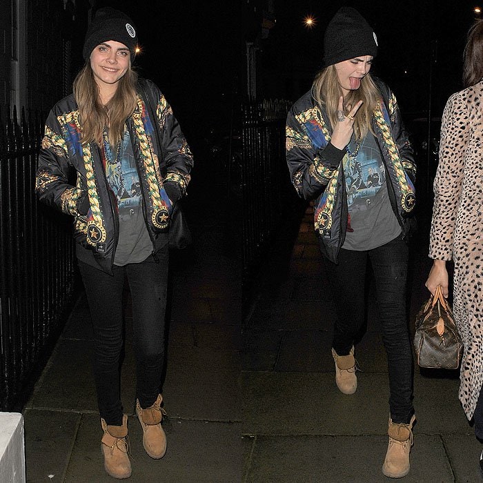 Cara Delevingne wearing Timberland boots with a beanie, a stadium jacket, a graphic tee, and skinny jeans