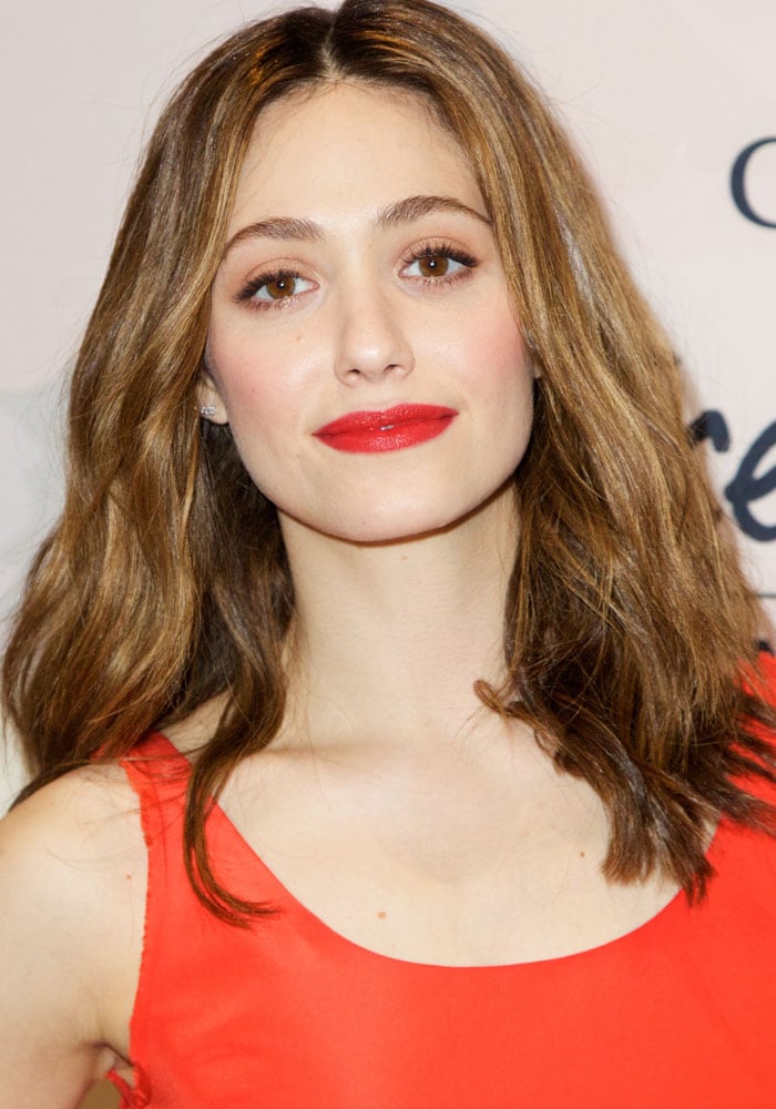 Emmy Rossum radiated elegance with her meticulously styled waves, subtle yet enhancing eyeshadow, and a vibrant red lip that perfectly complemented her tangerine ensemble at the Variety Power of Women luncheon