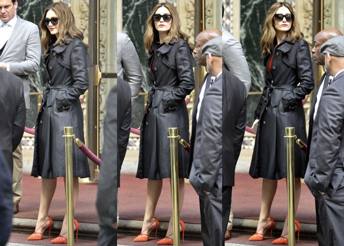 Emmy Rossum transitions effortlessly from her bright event attire to a sophisticated charcoal trench coat, adding an element of chic practicality while still showcasing her vibrant Louboutin 'Riri' heels and sunglasses for an understated elegance